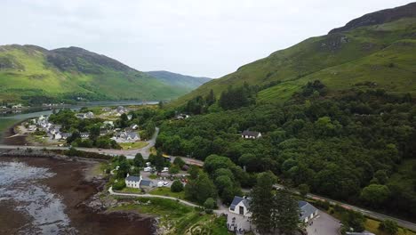 Dornie-town-reveal-behind-Eilean-Donan-castle,-Scotland,-aerial-drone-view