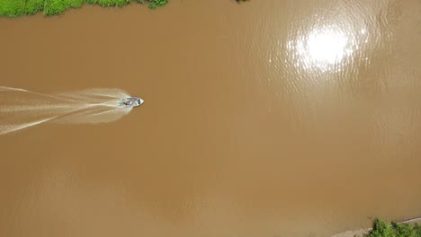 Top-down-aerial-view-of-people-riding-boat-in-murky-Indonesian-jungle-river