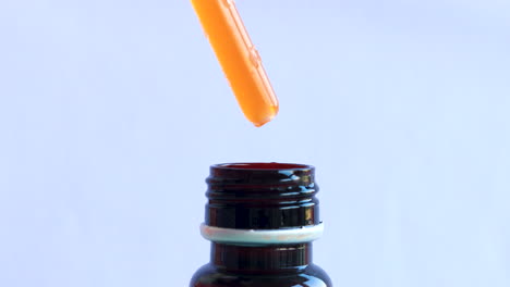 Isolated-close-up-of-pipette-pushing-out-orange-liquid-drops-into-brown-bottle
