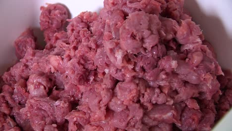 Pieces-of-red-minced-meat-pile-up-in-white-container,-closeup-in-butchery