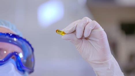 A-female-pharmaceutical-worker-examining-an-orange-gel-capsule-in-a-laboratory