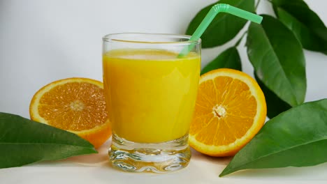 Close-up-studio-shot-of-full-glass-of-orange-juice-and-orange-halves,-fast-pan