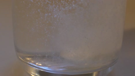 Slow-motion-close-up-of-white-tablet-dropping-into-clear-drinking-glass-of-water-and-dissolving-into-a-fizz-cloudy-liquid