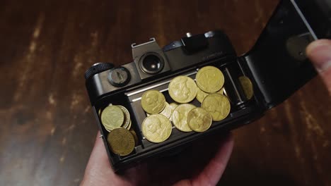 Camera-back-opened-by-Caucasian-hand-to-reveal-gold-coins-earned-by-the-camera