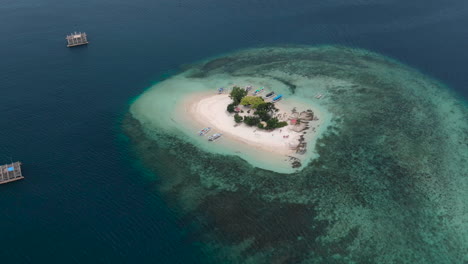 Aerial-orbital-shot-of-a-lonely-small-white-sand-island,-a-coral-reef-in-the-transparent-blue-clean-ocean
