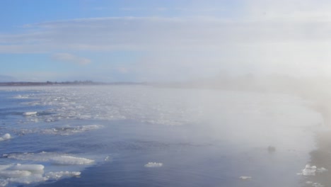 Weißer-Rauch-Zieht-Durch-Den-Isländischen-Blauen-See-Mit-Schwimmenden-Schmelzenden-Gletschern-Unter-Strahlend-Blauem-Himmel---Schwenk-Nach-Links