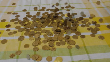 Many-coins-fall-from-above-on-top-of-a-yellow-and-green-bed-spread,-close-up