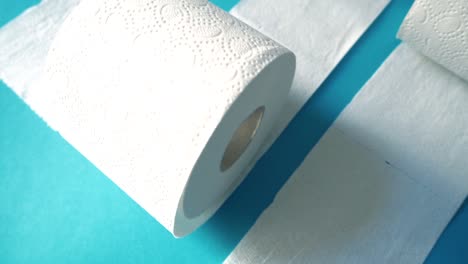 Slow-motion-of-several-rolls-of-toilet-paper-against-a-cyan-blue-modern-background