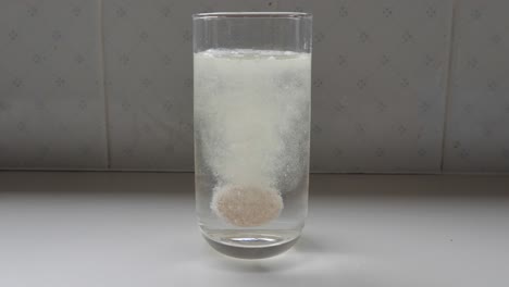Cámara-Lenta-De-La-Tableta-De-Disolución-De-Naranja-Caída-En-Un-Vaso-De-Agua-Y-Burbujeando-Con-Burbujas