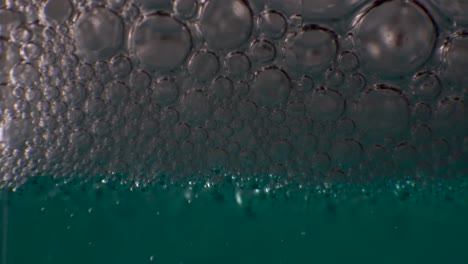 Thick-layer-of-clear-bubbles-gathering-on-top-of-aqua-colored-liquid,-MACRO