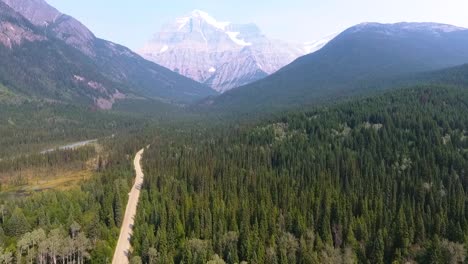 Ascending-aerial-drone-shot-of-wilderness,-mountains-as-a-road-cutting-through-the-forest