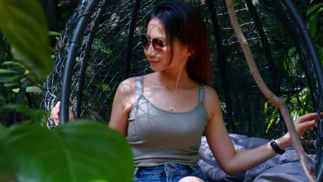 Asian-Girl-Wearing-Sunglasses-Sitting-In-Hanging-Chair-In-Lone-Pine-Koala-Sanctuary,-Brisbane,-Australia