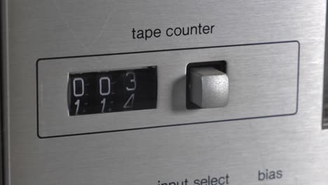 Side-perspective-of-stereo-hifi-casette-tape-counter-counting-up-with-black-digit-numbers-ticking-over-and-silver-metal-button-off-to-side