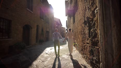 Retro-couple-walking-in-rustic-street-in-Tuscany-holding-hands-at-sunrise