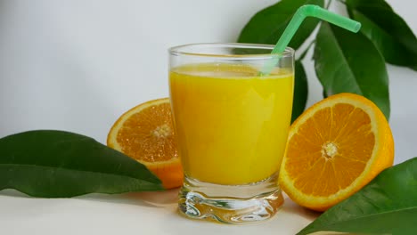 Close-up-studio-shot-of-full-glass-of-orange-juice-and-orange-halves,-slow-pan