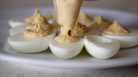 Hands-of-caucasian-male-filling-boiled-egg-whites-with-creamy-egg-yolk-mixture-using-plastic-piping-bag