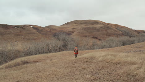 Ein-Erwachsener-Männlicher-Jäger,-Der-In-Richtung-Der-Dicken-Bürste-Am-Fuße-Eines-Kleinen-Hügels-In-Der-Nähe-Einer-Schnellen-Strömung-Geht,-Saskatchewan,-Kanada