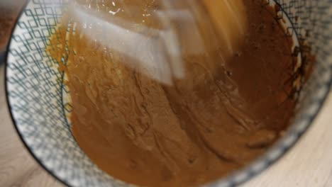 Woman-vigorously-mixing-dalgona-coffee-ingredients-with-hand-whisk,-closeup