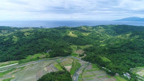 Wide-Panning-Aerial-Shot-Of-A-Farm-Beside-The-Mountains,-Nearby-Sea