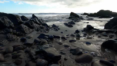 Ocean-water-crashing-onto-beach-with-rocks-during-low-tide-on-sunny-day