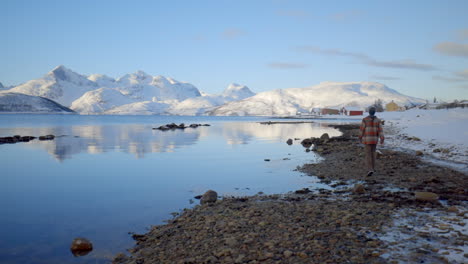 Un-Hombre-Caminando-Sobre-Una-Tranquila-Línea-Costera-Nevada-A-Lo-Largo-De-Un-Fiordo-En-Noruega-Con-Un-Paisaje-Invernal-Asombroso,-Estático