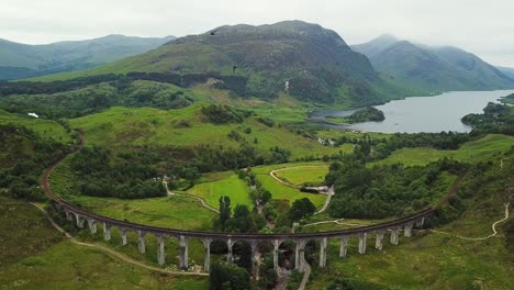 Jacobite-steam-train-approaching-Glenfinnan-Viaduct-as-swifts-fly-near-camera,-aerial