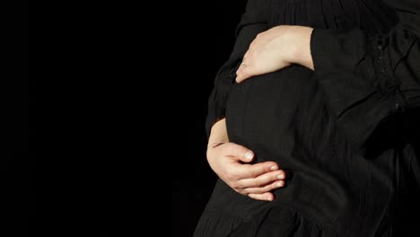 A-pregnant-woman-gently-holds-and-rubs-her-round-belly-with-copyspace-against-a-black-background