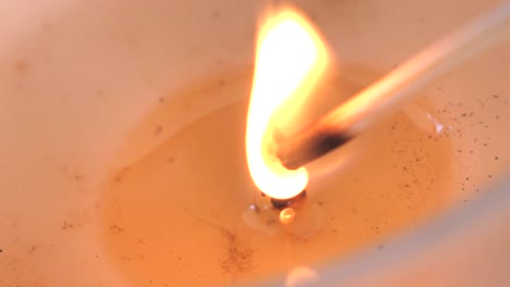 Slow-motion-macro-footage-of-candle-wick-being-lit-by-wooden-match-to-burn-with-bright-orange-flame-flickering-in-soy-wax
