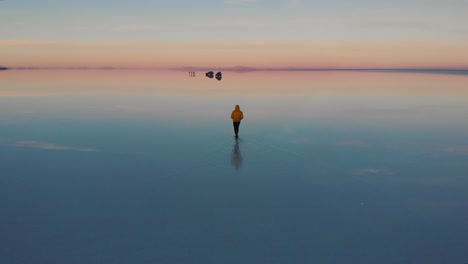 A-young-man-with-a-yellow-jacket-walking-on-flooded-salt-flat-in-bolivia-during-sunrise