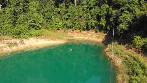 Paddling-Across-The-Beautiful-Turquoise-Lake-Neath-The-Lush-Green-Forest-Mountain-In-Thailand---Mavic-Drone-Shot