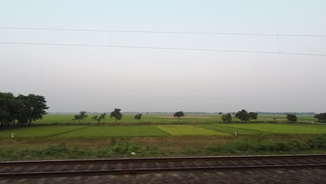 Large-agricultural-farm-land-and-paddy-field,-shot-through-fast-moving-train