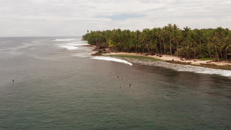 Aerial-flight-towards-surfers-floating-in-ocean-by-Indonesian-palm-beach