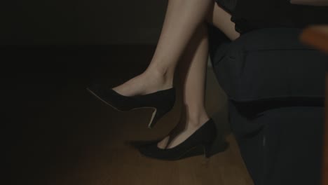 Close-up-of-women's-legs-with-black-high-heels-sitting-down,-crossing-her-legs-and-dangling-her-feet