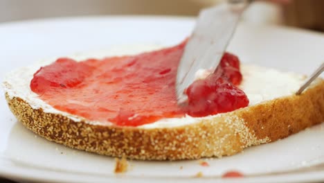 Close-up:-silver-knife-spreads-and-puts-on-strawberry-jam-on-buttered-bread-slice