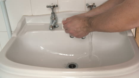 Male-hands-wash-and-scrub-with-soap-for-twenty-seconds-in-a-white-bathroom-sink