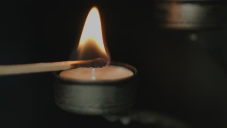 Nahaufnahme-Eines-Teelichts-In-Einem-Silbernen-Kerzenhalter,-Das-Nachts-Von-Einem-Flackernden-Streichholz-Mit-Dunklem-Hintergrund-Beleuchtet-Wird