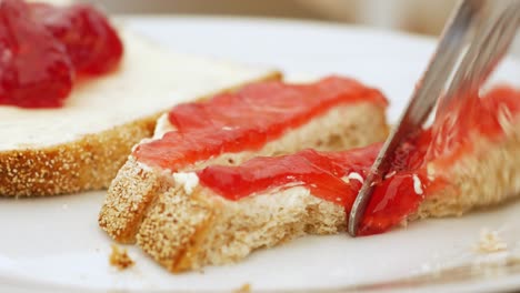Strawberry-jam-and-buttered-bread-is-cut-into-narrow-slices-on-white-dish,-close-up