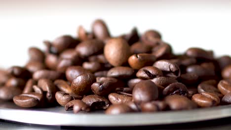 Pouring-cup-of-roasted-golden-brown-coffee-beans-on-top-of-round-silver-scale