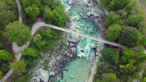 Wide-aerial-shot-of-untamed-mountain-river-flowing-below-bridge-in-spring