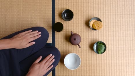 Hombre-Sentado-En-Una-Alfombra-De-Tatami-Comiendo-Galletas-Y-Bocadillos-Japoneses-Tradicionales-Durante-La-Hora-Del-Té---Tiro-Medio