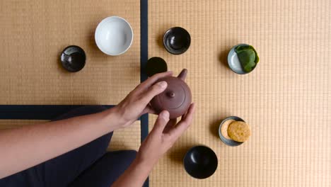 Mann-Schüttelt-Teekanne,-Während-Er-Auf-Dem-Tatami-Boden-In-Einem-Japanischen-Haus-Sitzt---Nahaufnahme