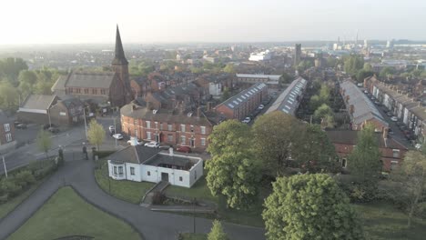 Drone-dolly-left-view-across-British-church-steeple-and-town-public-park-houses-at-sunrise