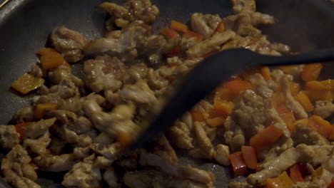 Plastic-spatula-flipping-pieces-of-chicken-shoarma-with-bell-pepper-in-frying-pan---close