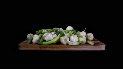 Push-In-shot-of-Fresh-White-Onions-Over-A-Wooden-Cutting-Board-On-Black-Background-at-eye-level