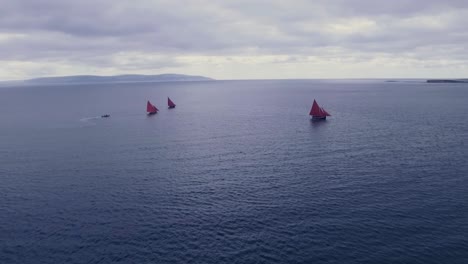 Aerial-Shot-of-Three-Boats-with-Red-Sails-moving-Out-to-Sea