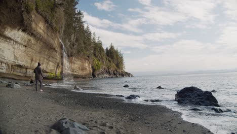 Ein-Mann,-Der-Am-Sandufer-Läuft-Und-Die-Hände-In-Die-Luft-Hebt-Und-Spaß-Am-Mystischen-Strand-Mit-Wellen-Hat,-Vancouver-Island,-Bc,-Kanada