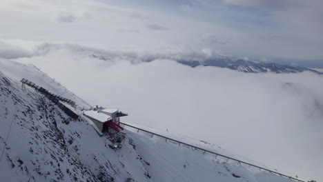 Aerial-top-down-shot-of-Lift-on-snowy-mountain-peak-above-clouds-in-winter---Austria,Europe