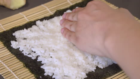 Hände-Eines-Kochs,-Der-Eine-Dünne-Schicht-Weißen-Reis-Auf-Das-Nori-Blatt-Legt-Und-Sanft-Drückt