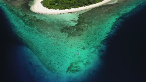 Banca-boat-floating-near-Mantigue-Island-in-the-Philippines,-tilt-up-aerial