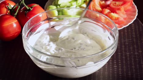 Onion-sour-cream-sauce-in-glass-bowl-is-mixed-with-silver-spoon,-close-up